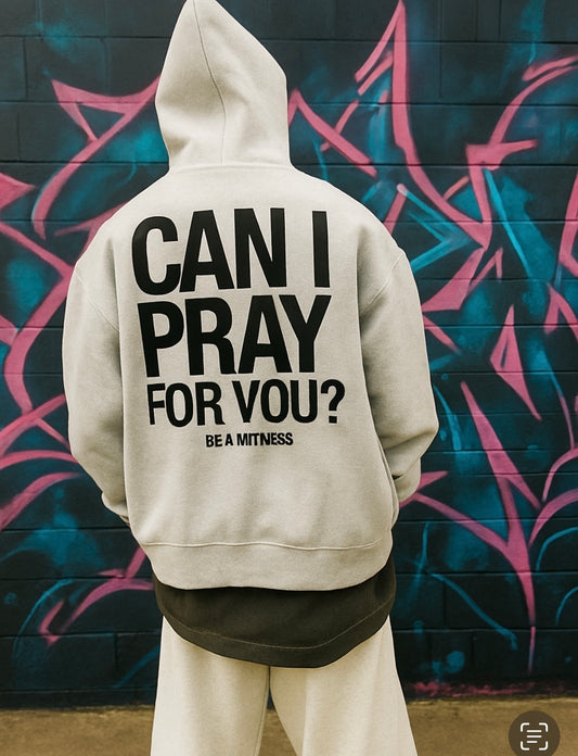 Person wearing a hoodie with text 'CAN I PRAY FOR YOU? BE A WITNESS' against a graffiti-covered wall.